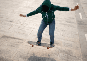A person with green jacket enjoys maneuvering his skateboard during cold season. 