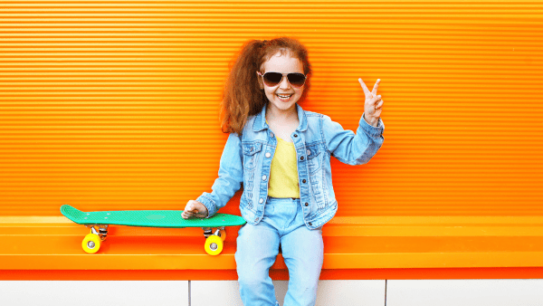 Skater kid sits beside her skateboard for skateboarding. 