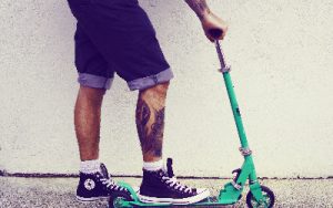 A man with a tattoo on his right leg holds his scooter for his fitness routine. 