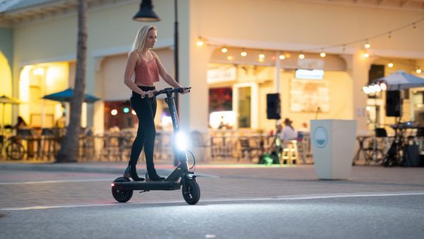A girl in a night scooter riding on a city street. with LED light on. 