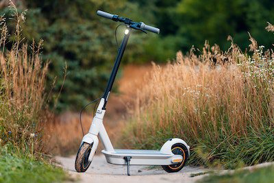 An electric scooter parked in the middle of a field with overgrown grass around. 