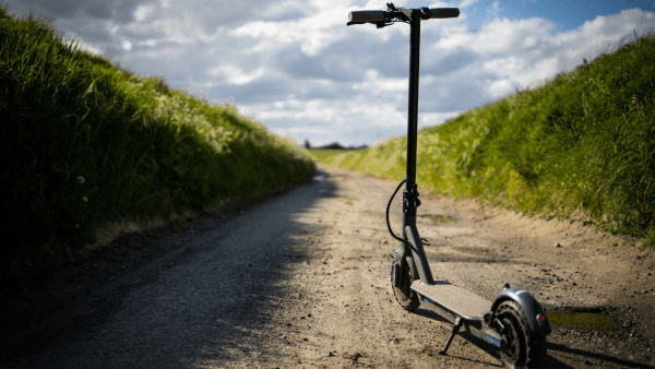 There is an electric scooter on the road with green fields on the side.