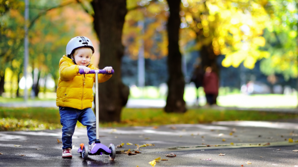 A three years-old kid riding a scooter. 