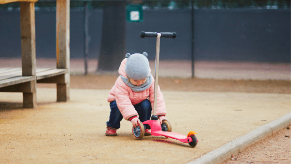 A toddler touching the two wheels of the scooter. 