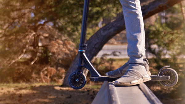 A kick scooter and a rider wearing skinny jeans and shoes. 