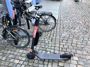 Electric scooters for kids parked on a cobblestone street next to bicycles, showcasing a modern and convenient transport option for children.