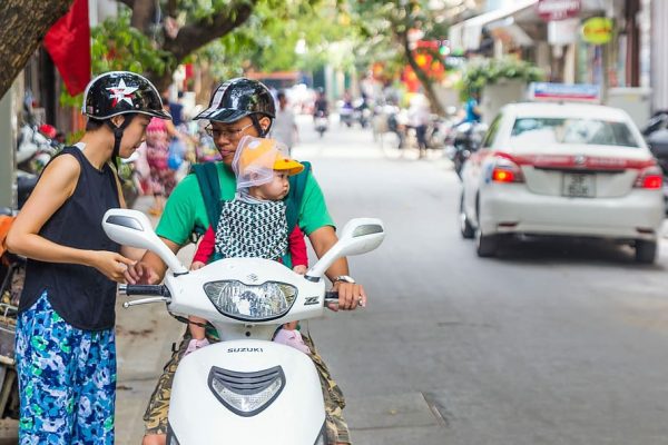 A couple with their kid riding a scooter. They are wearing helmets for their safety.