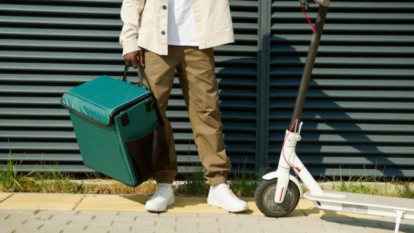 Scooter in style. A man with a delivery bag, next to a kick scooter. A scooter offers an easy, and convenient way to travel. Get into scooter lifestyle. Ride a scooter and see the difference yourself. 