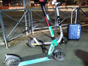 Two e-scooters are in the street with travel luggage.