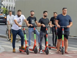 Six scooter riders in the street, zipping joyfully.