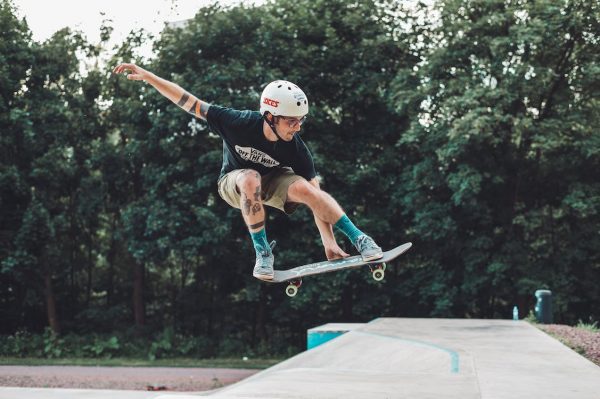 A skateboarder practicing his skateboarding tricks at the skatepark. He is wearing the appropriate skateboard safety gear to keep himself safe while skating.
