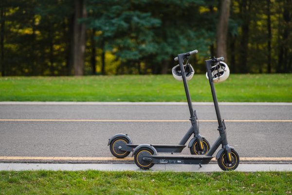 Electric scooters are parked on a sidewalk with matching helmets that are hanging from the handle.