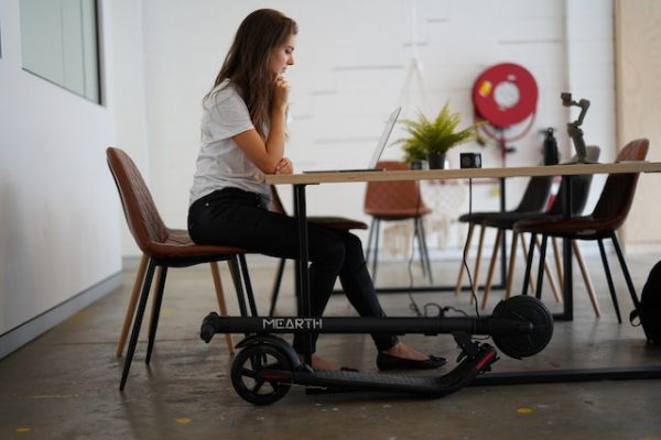 A woman working on her laptop, with her foldable scooter by her side. 