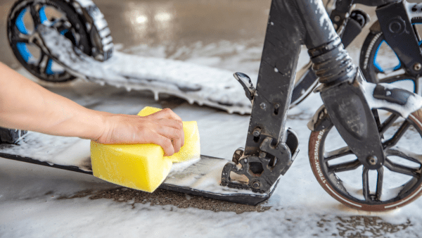 A hand holding a sponge washing the dirty e-scooter