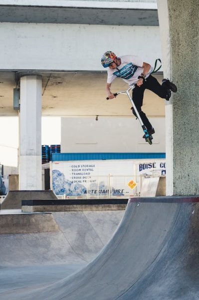 A man doing scooter stunts on a half-pipe in a skate park