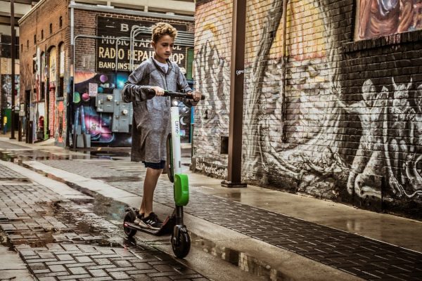 A boy in a raincoat riding a scooter on a wet street