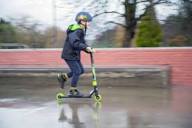 A boy playing with his scooter and wearing safety gear in the park