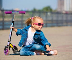 Smiling child wearing sunglasses, sitting beside a colorful foldable scooter