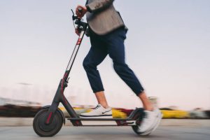 Deck: The photo captures a dynamic moment of a person riding an electric scooter, with the scooter deck in motion, set against a blurred cityscape during what appears to be twilight hours, emphasizing the sense of speed and urban commuting. The scooter deck is flat. The scooter deck is flat.