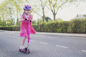 young girl riding a scooter on the road with complete gears like helmet, knee pads, and more