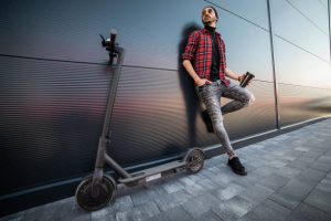 Man wearing street style fashion is standing beside his scooter after taking a long ride around the cityscape. There’s a unique sense of bliss or happiness when riding.