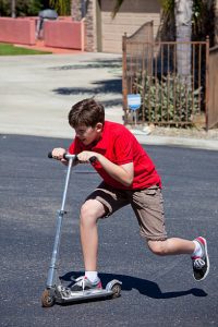 riding a scooter to a road that seems inclined: boy pushing himself to ensure he gets to the top or his destination