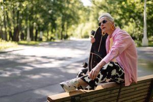  A woman seated next to a skateboard ready for skateboarding.