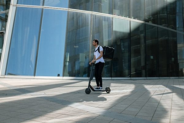 A man carrying a backpack while riding a scooter