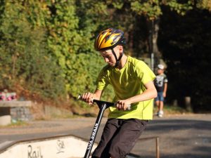  A teenager with a yellow helmet practices his spinning while riding his scooter.