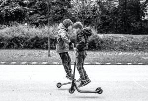 Two kids riding a scooter doing scooter flip with their scooter that has the same feature