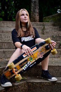 Skateboard: A young individual sitting on steps outdoors, holding a well-used street skateboard, possibly considering a new skateboard buying guide.