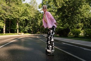 An elderly woman confidently rides her skateboard.