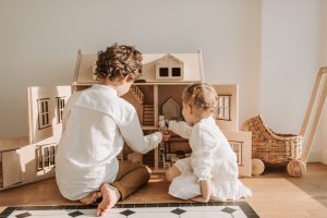 Kids playing with wooden doll house with fixtures and accessories.