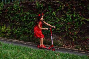 A little girl riding scooting outside. Riding a scooter can be very fun. Scooting can be done around your neighborhood by a preschooler. 