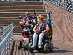 Two persons riding mobility scooters while talking to each other. 