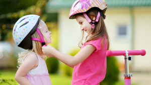 Two girls are gearing up to ride their scooters.