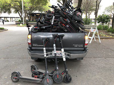 Scooters with big wheels are on the black car of a parent-owner ready for delivery to a buyer.