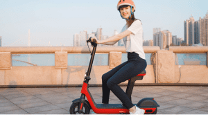 A woman wearing a white shirt rides her red scooter safely along the bridge while on her way home. 