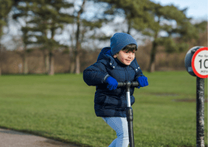 A boy rides outside and uses gloves for a scooter