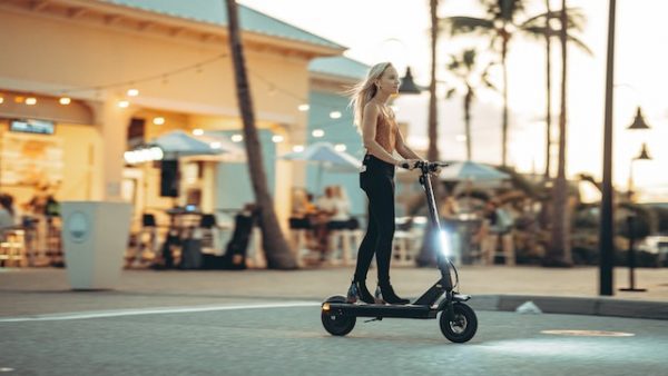 A blond-haired woman is enjoying her scooter ride outside a store while her hair is touched by the wind.