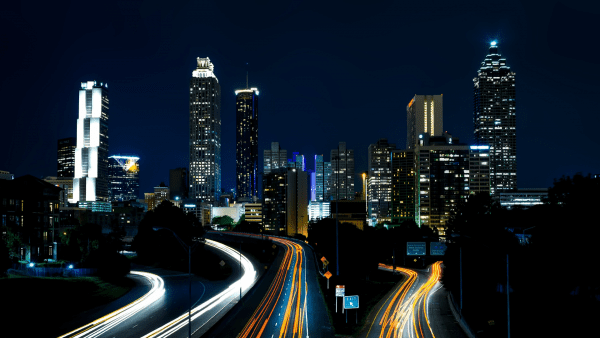 It is nighttime. The sky is so dark but many buildings with bright lights give life to the picture. You can see that each building has its own unique style. You can see at the bottom that there are also lights that form many trail lines. These lights could be moving vehicles. The photographer of this picture used the technique called a light trail. This technique is very common in a busy highway. They capture it by setting the long exposure in the camera.