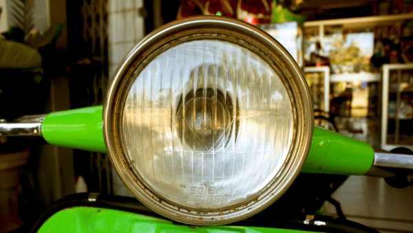 Here is one more picture of a scooter's light. The motorbike is painted in an extremely bright shade of green that is super eye-catching. The green color is so bright that it's hard to miss, like a color that wants to say, "Look at me!" The light coming from the scooter adds to the coolness of the picture. Imagine how cool it would be to ride around on a scooter like this, with a light that shines so brightly, especially at night. This scooter seems to be saying, "I'm here and I'm ready to zoom around with style!"