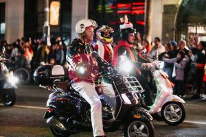 A person riding a scooter safely at night. They wear a reflective helmet, fluorescent jacket, and illuminated wristbands.