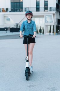 A woman in a blue shirt wears her helmet while maneuvering her scooter. 