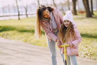 Mother and daughter wear winter clothes while playing outdoors. 