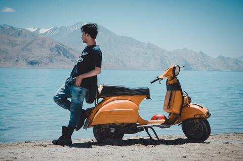 Young man leaning on his motorcycle in front of a lagoon
