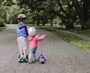 Two kids with helmet ride their scooters while enjoying the view outdoors. 