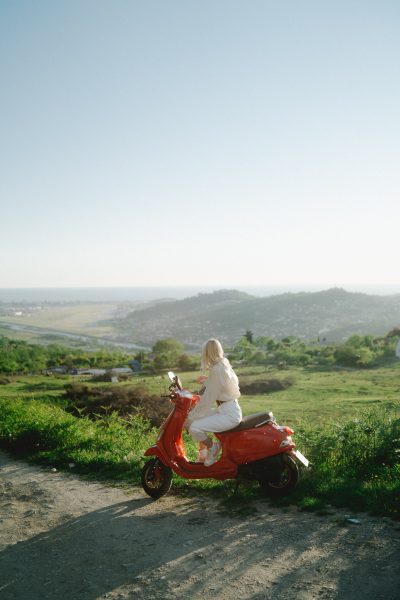 A rider with a red e-bike sits on top of the mountain looking at the magnificent view below, a lush green landscape connecting one mountain to the others. 