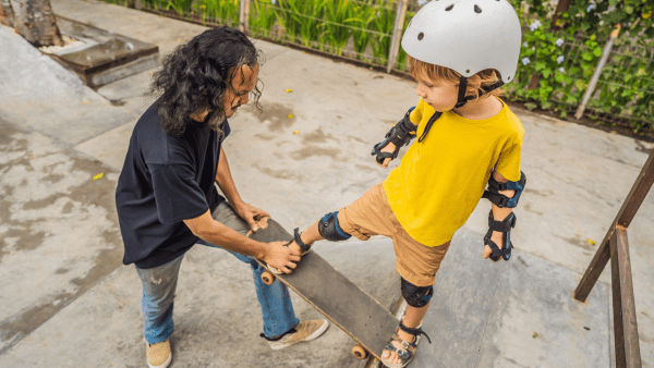 Skateboard experience. Helping a child riding a skateboard in the park. A kid wearing a skateboard gear with his skater dad. 