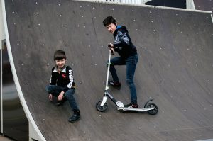 Kids wearing black jackets, having a blast as they perform stunts with a scooter. Their excitement doing stunts with scooter shows their adventurous side.